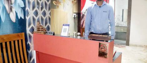Mostrador de recepción de hotel con un anuncio de Coca-Cola al fondo, un código QR para pagos y un cartel de prohibición de fumar.
