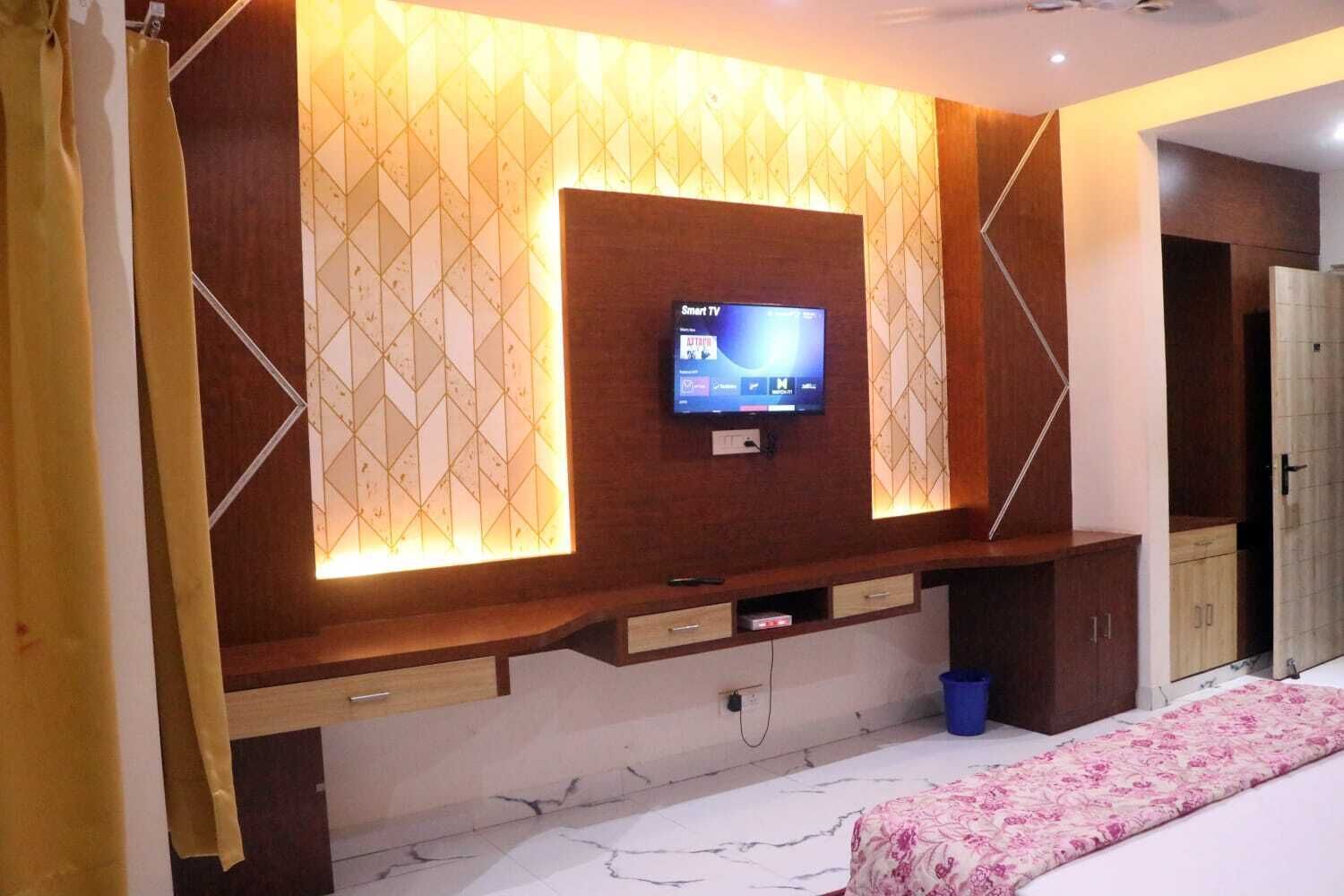 Un dormitorio con televisión montada en una pared con diseños geométricos, cama con colcha floral y un mueble de madera.