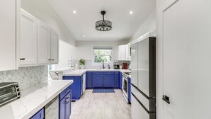A modern kitchen with white cabinets, blue accents, a marble backsplash, and a central island. - Kalispell Gem: Deck, Yard & Fireplace (Kalispell)