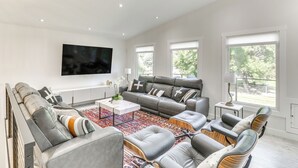 A modern living room with a grey leather sofa, a coffee table, and a flat-screen TV mounted on the wall. - Kalispell Gem: Deck, Yard & Fireplace (Kalispell)