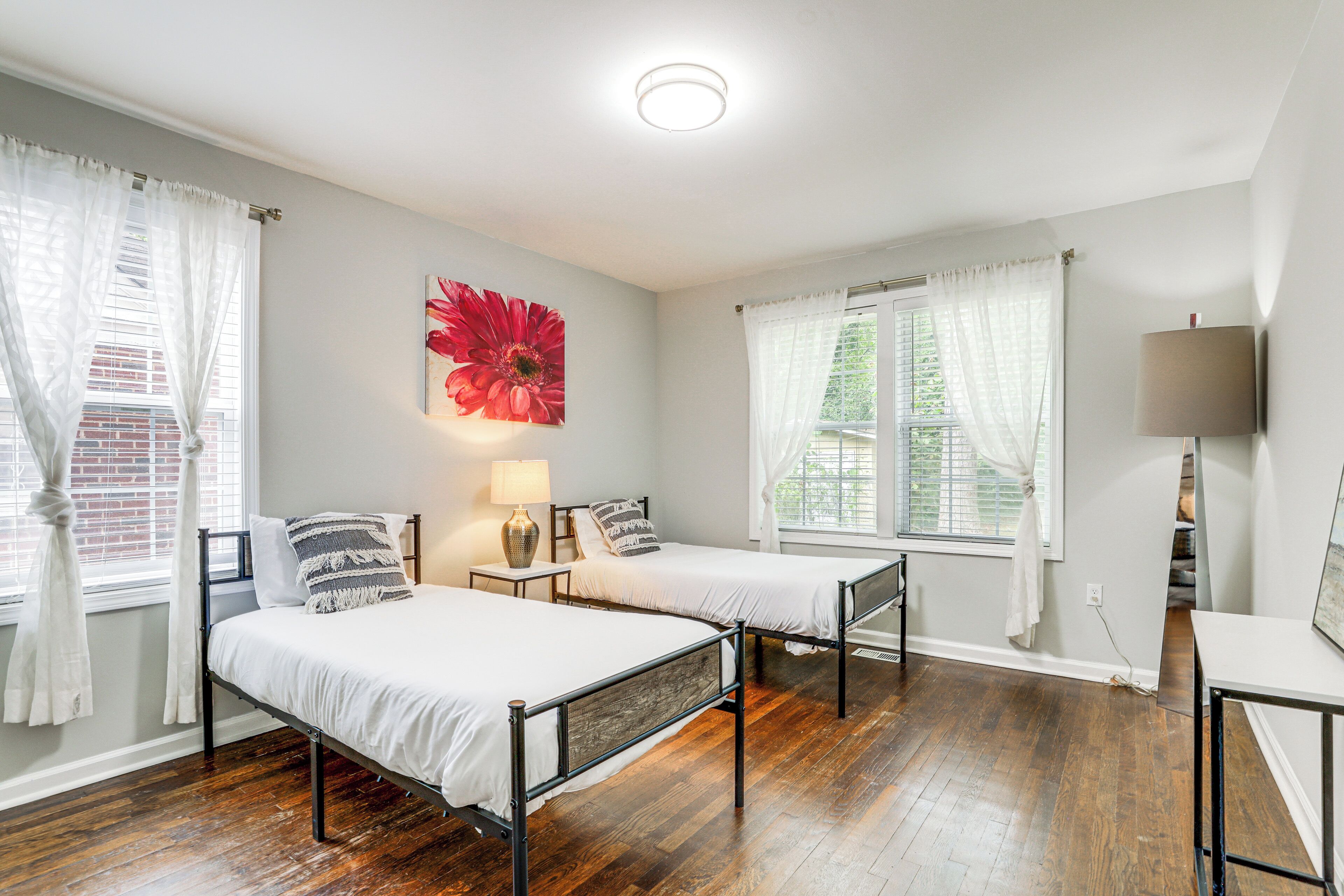 A room with two beds, a lamp, and a large flower painting on the wall.