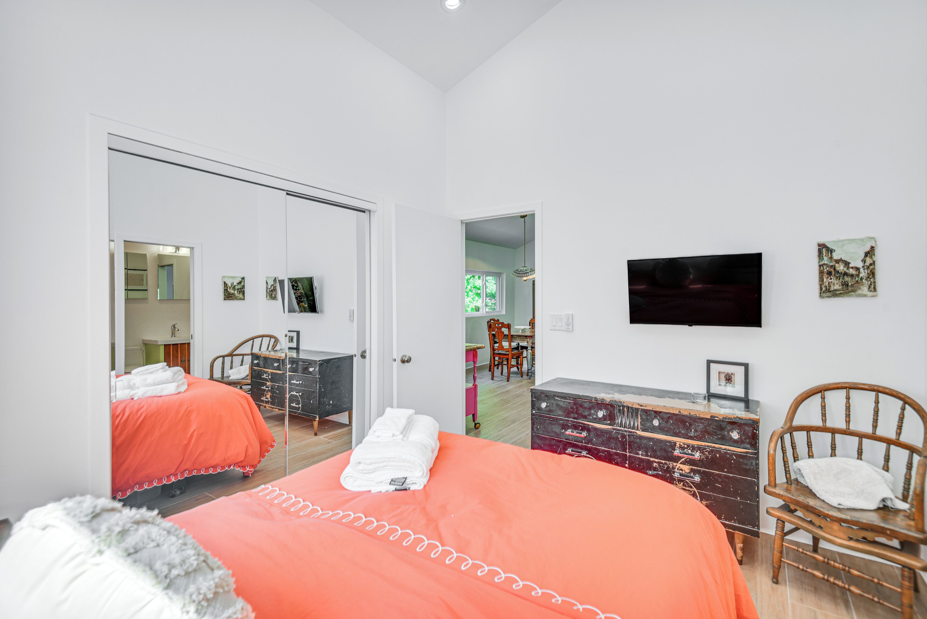 Un dormitorio con dos camas, un tocador, una silla, un televisor y una puerta que da a otra habitación.