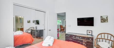 Un dormitorio con dos camas, un tocador, una silla, un televisor y una puerta que da a otra habitación.