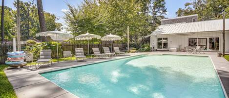 A rectangular swimming pool with a tiled deck, surrounded by lounge chairs and umbrellas.
