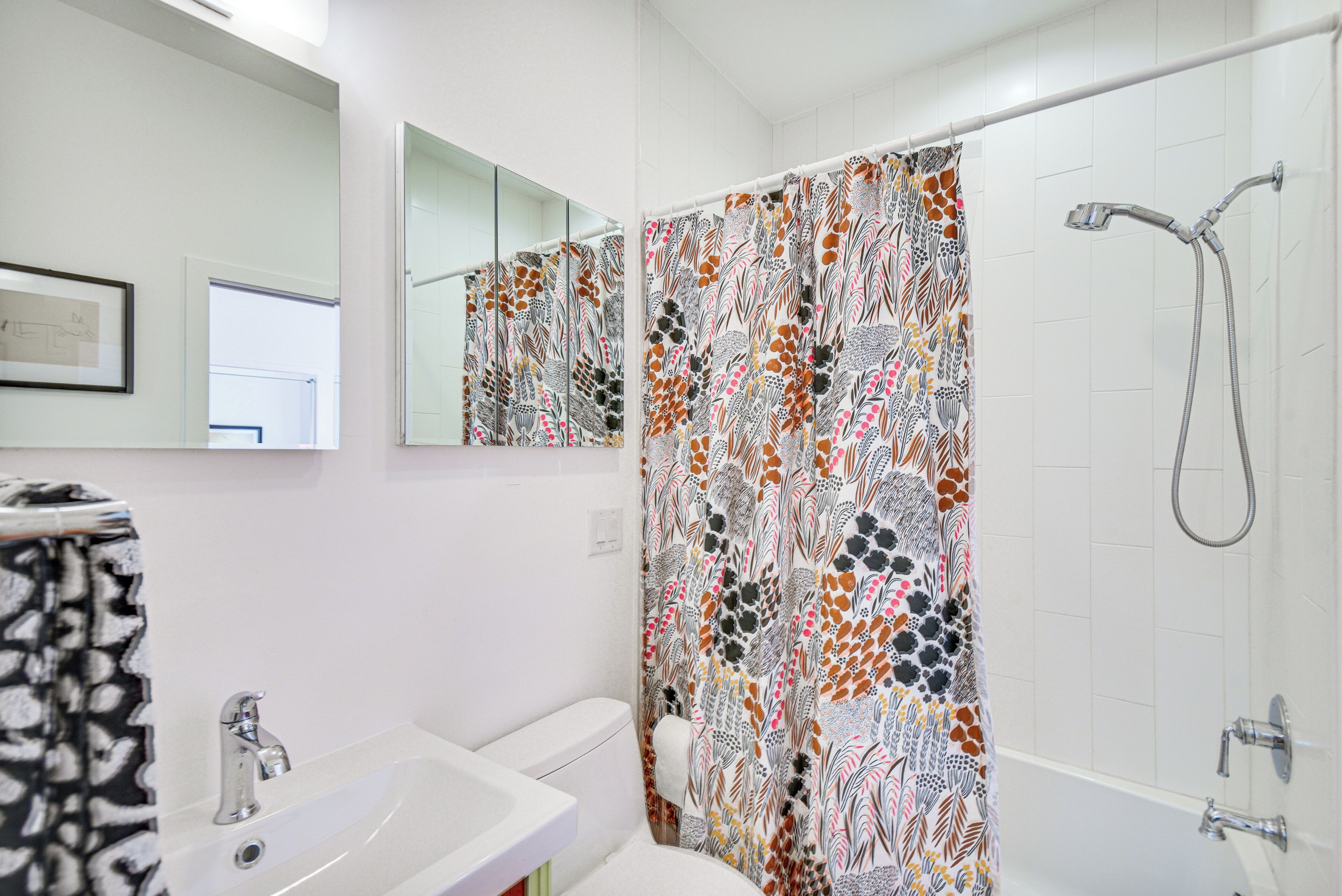 Een badkamer met een wit wastafelmeubel, een spiegel, een douche met een decoratieve gordijn en een toilet.