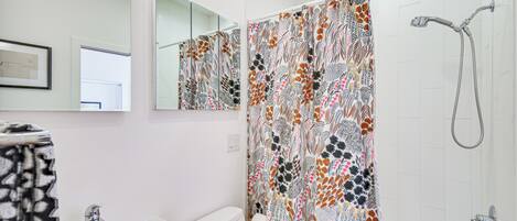 Een badkamer met een wit wastafelmeubel, een spiegel, een douche met een decoratieve gordijn en een toilet.