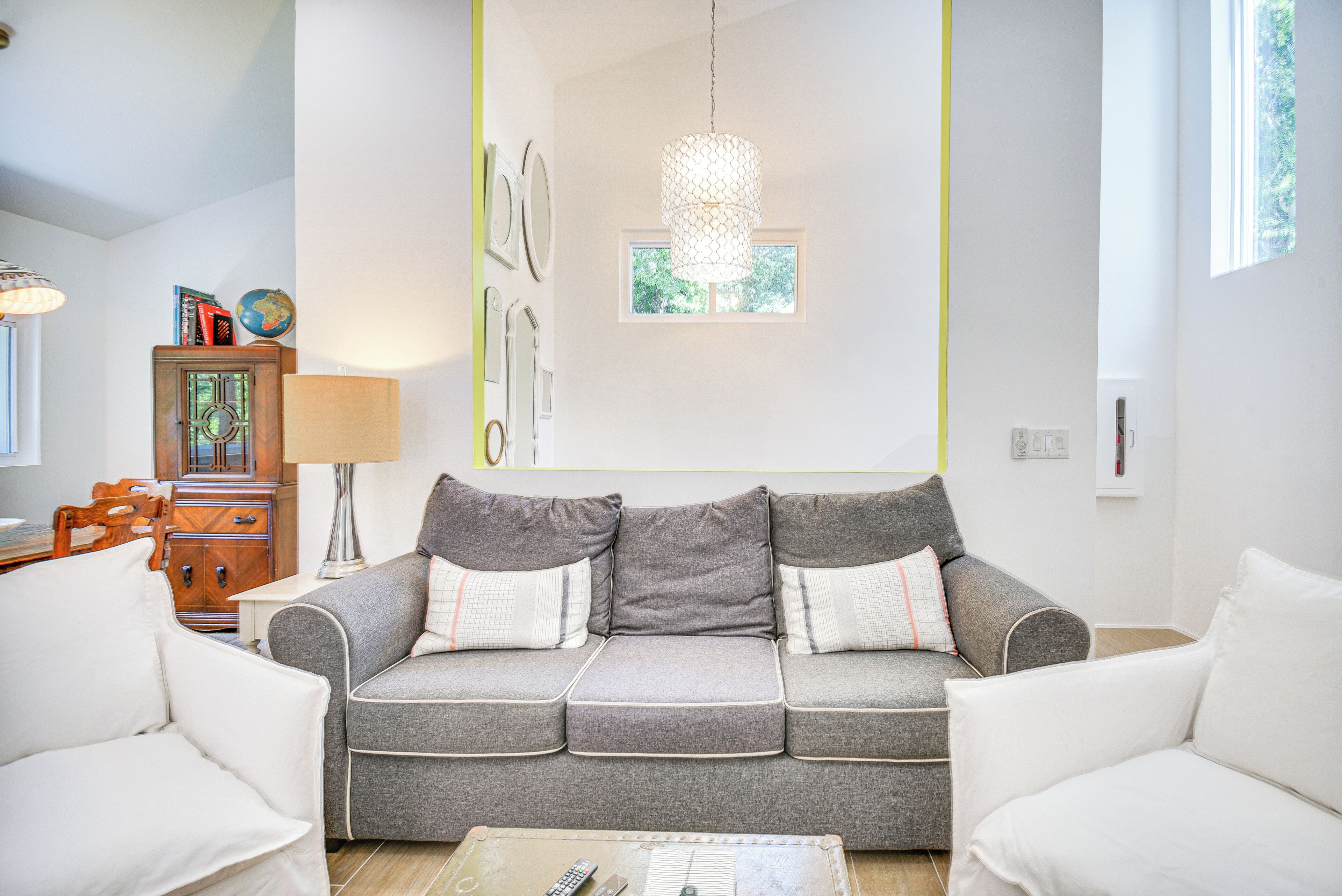 A living room with a grey sofa, white armchairs, a wooden cabinet, and a lamp.