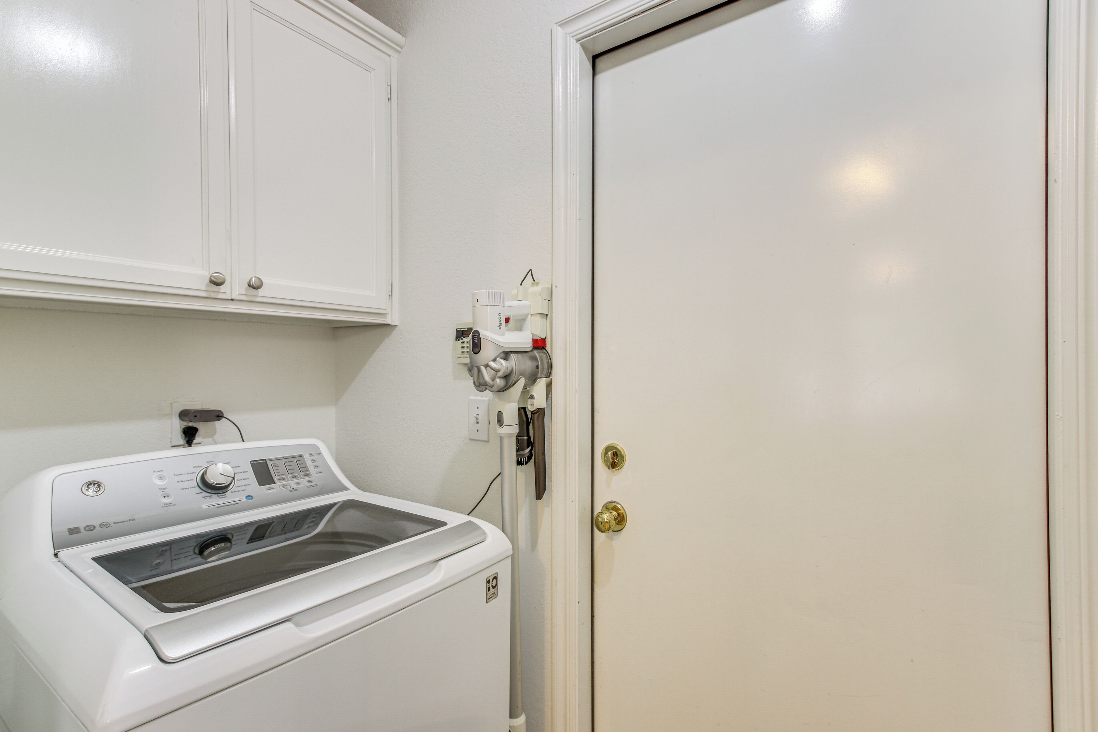 A laundry room with a front-loading washing machine, a dryer, and a door with a brass handle.