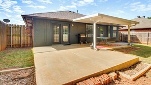 Un jardin avec un patio couvert, un barbecue et une zone délimitée par une clôture.