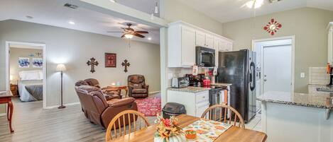 A spacious living room with a fireplace, a dining area with a wooden table, and a kitchen with white cabinets and modern appliances.