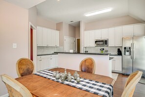 A modern kitchen with white cabinets, stainless steel appliances, and a wooden dining table with a checkered table runner. - Bryan Home: Close to Campus & Kyle Field (Bryan)