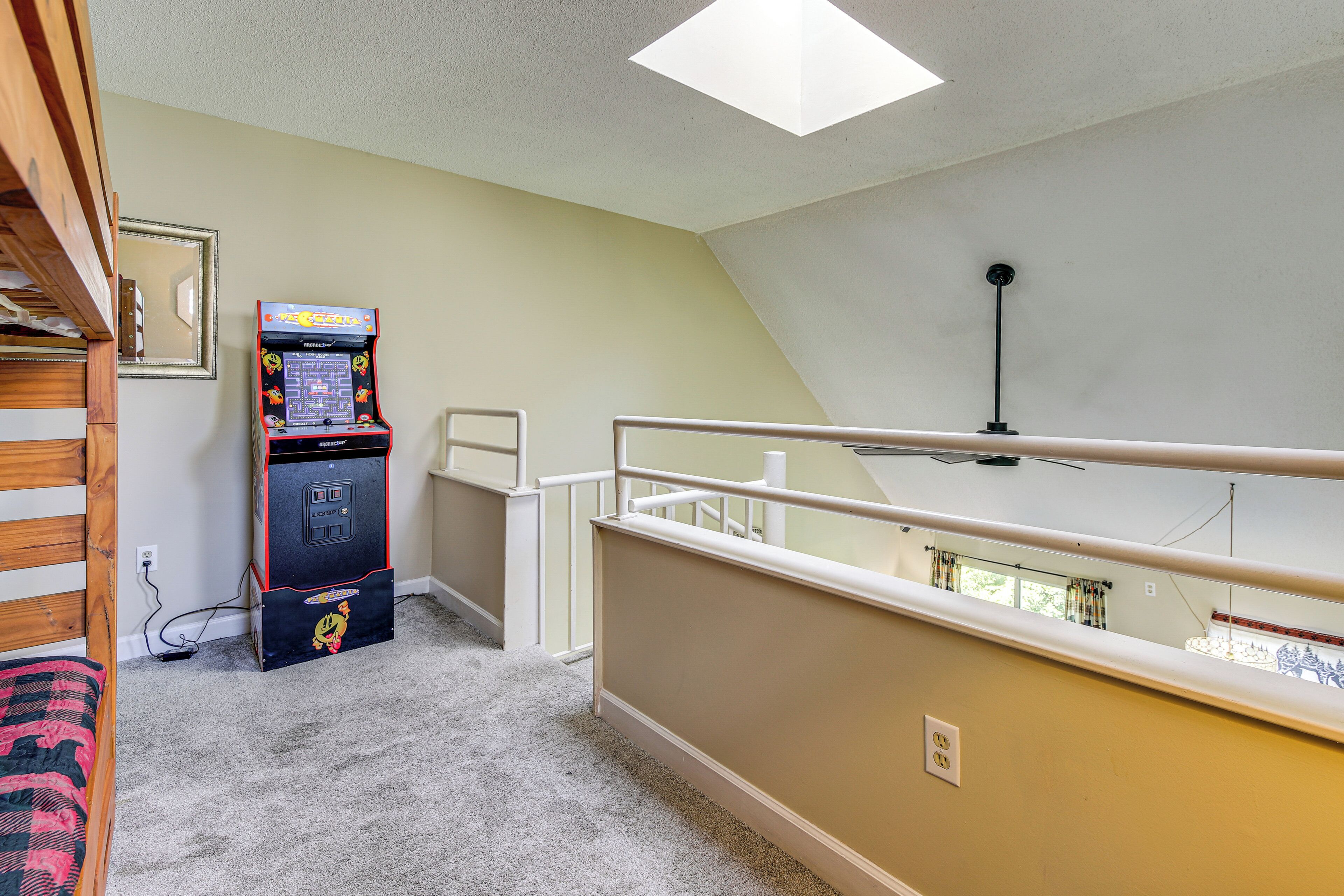 Una habitación con piso alfombrado, ventilador de techo, espejo en la pared y una máquina arcade pequeña.