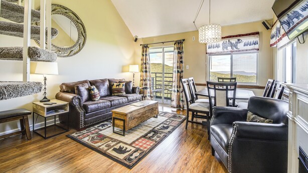 A living room with a brown leather sofa, wooden coffee table, and a patterned rug. There is a dining table with chairs and a chandelier. - 2 Mi to Ober Mountain: Gatlinburg Condo w/ Balcony (Gatlinburg)