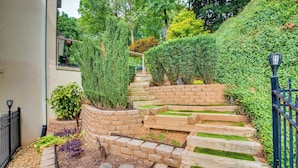 Un jardín ajardinado con un muro de piedra, escalones de madera y una cerca de metal.