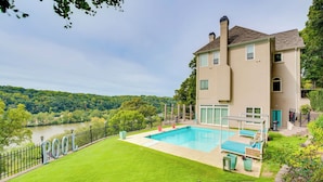 Una casa de dos pisos con piscina, césped cuidado y vista al río.