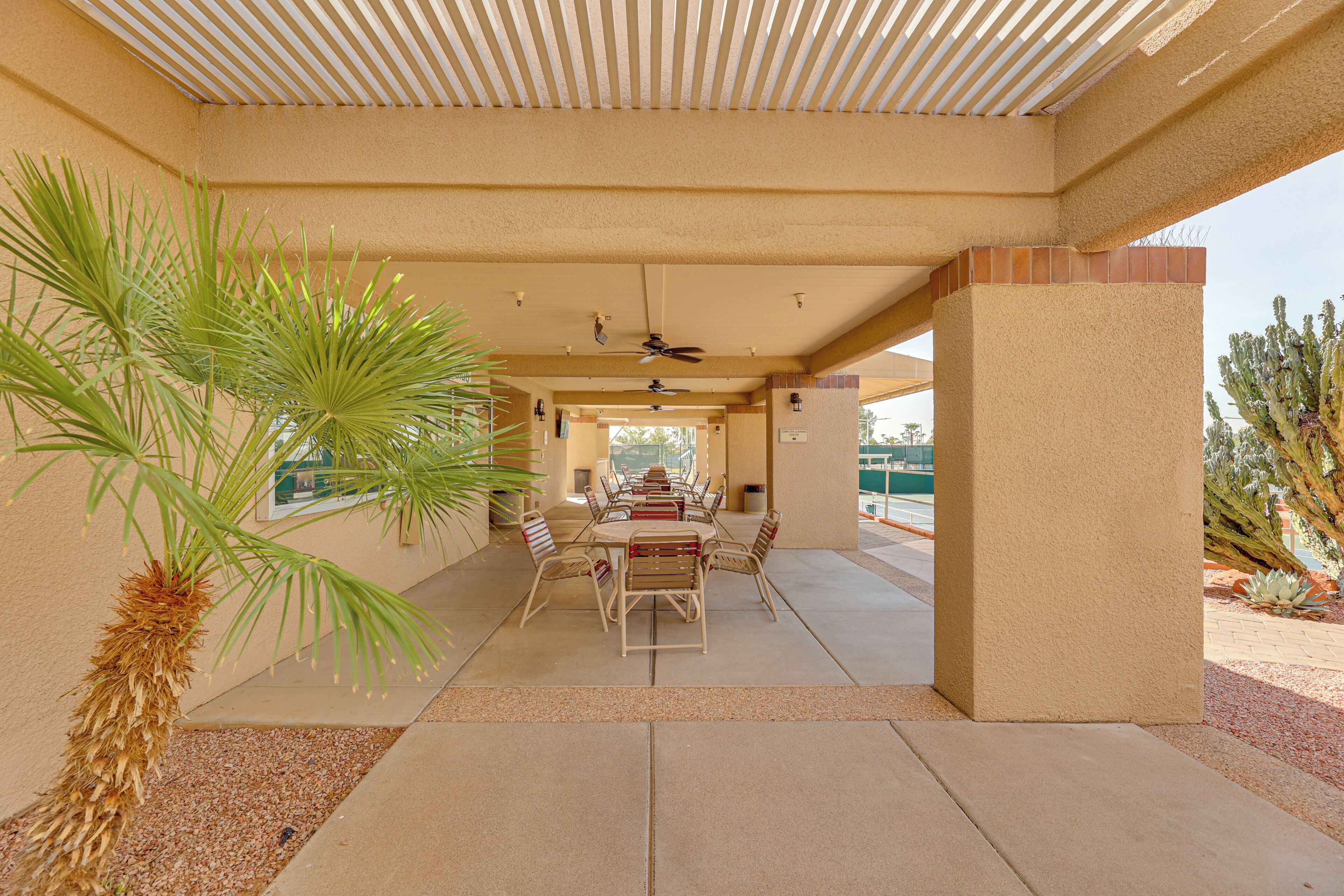 An outdoor patio with a table and chairs, palm trees, and a ceiling fan.