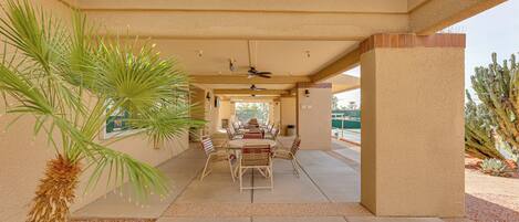 An outdoor patio with a table and chairs, palm trees, and a ceiling fan.