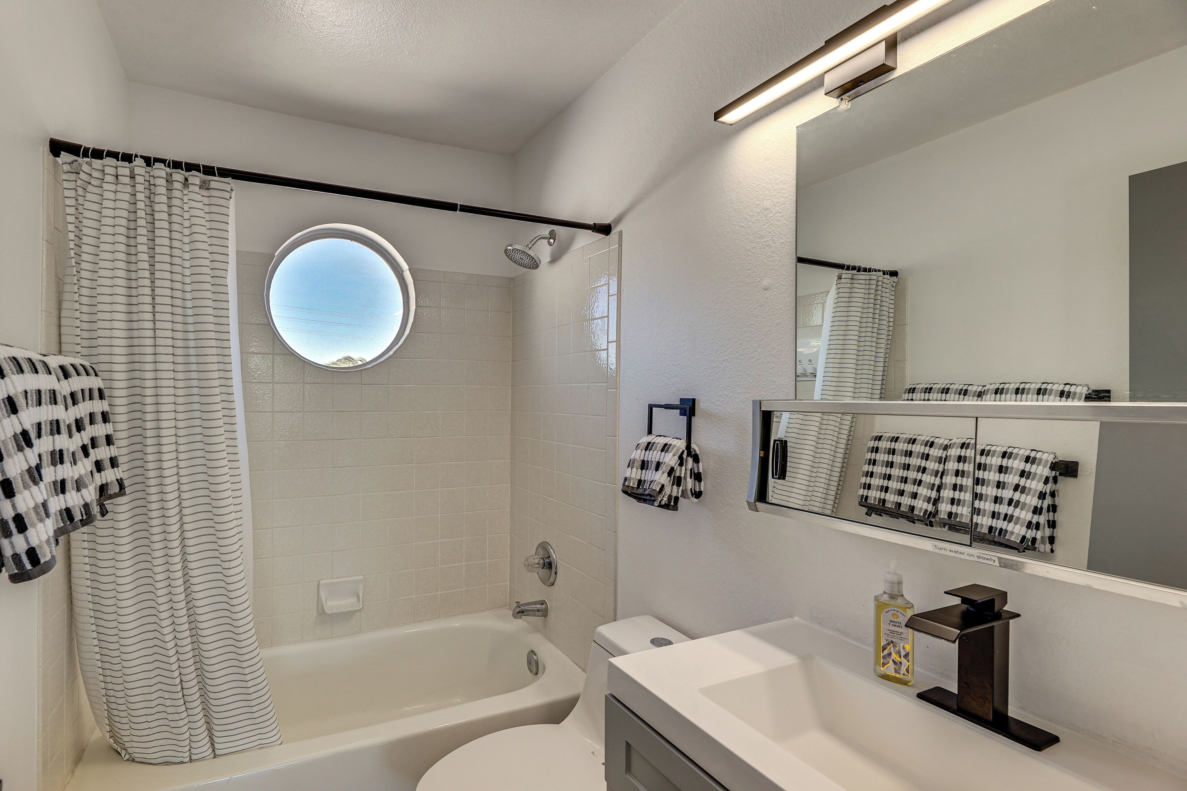 A modern bathroom with a bathtub, toilet, and a round mirror.