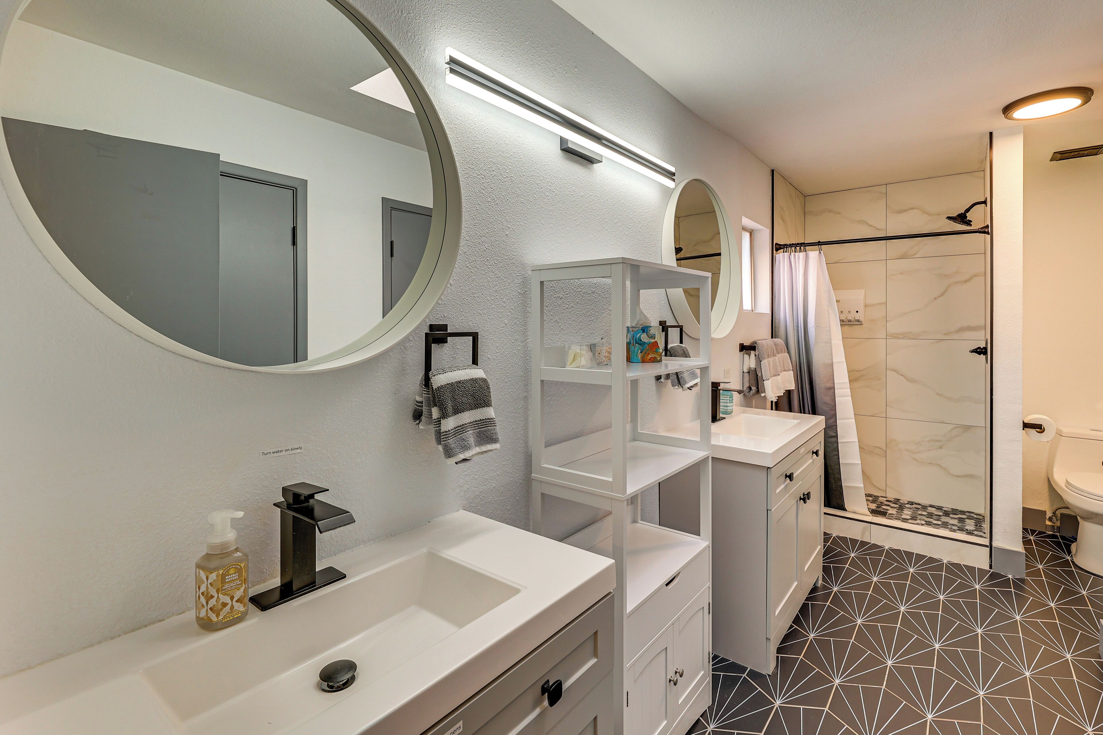 Un baño moderno con tocador blanco, un espejo grande y zona de ducha.
