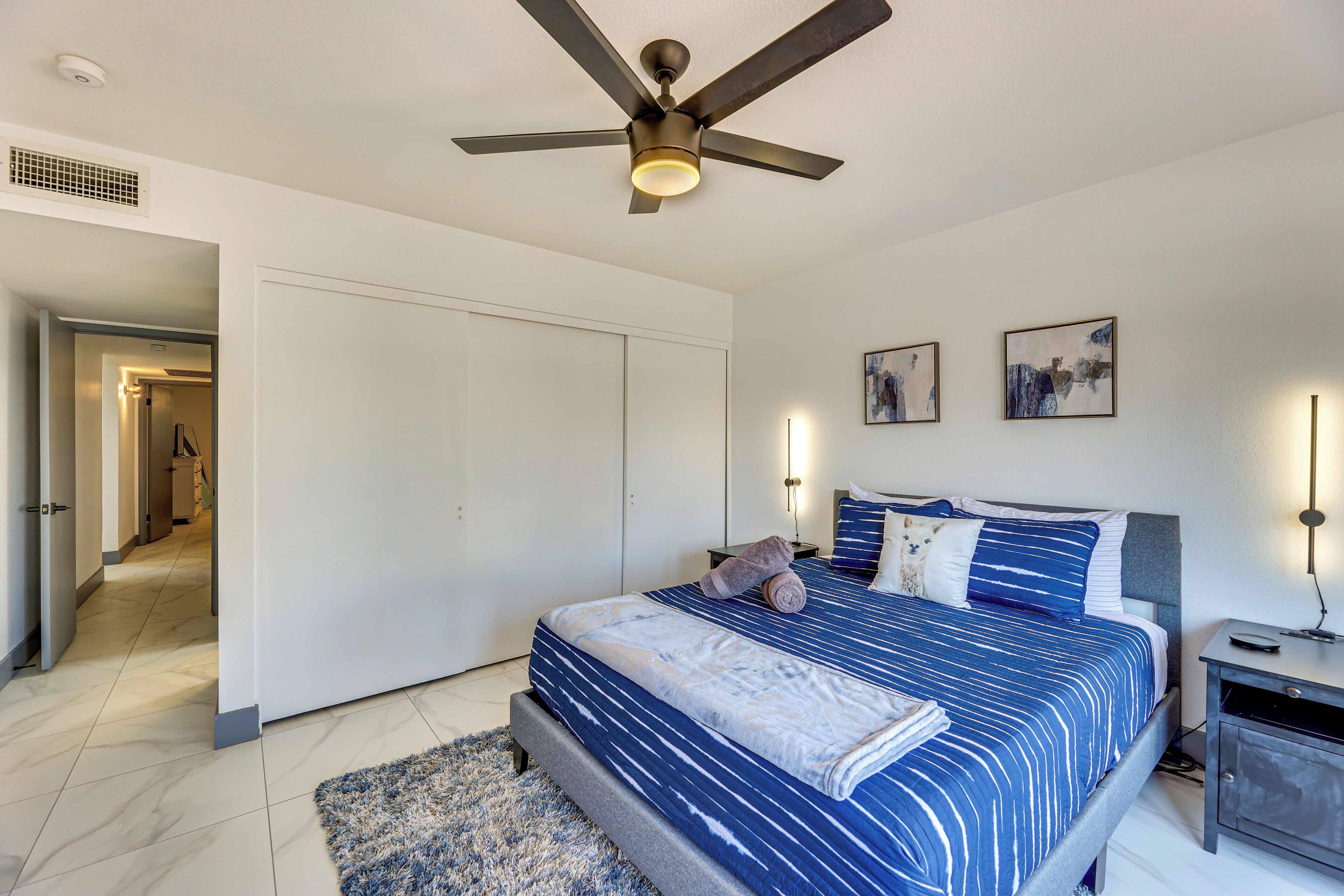 A bedroom with a bed, a ceiling fan, a nightstand, and a wall-mounted light.