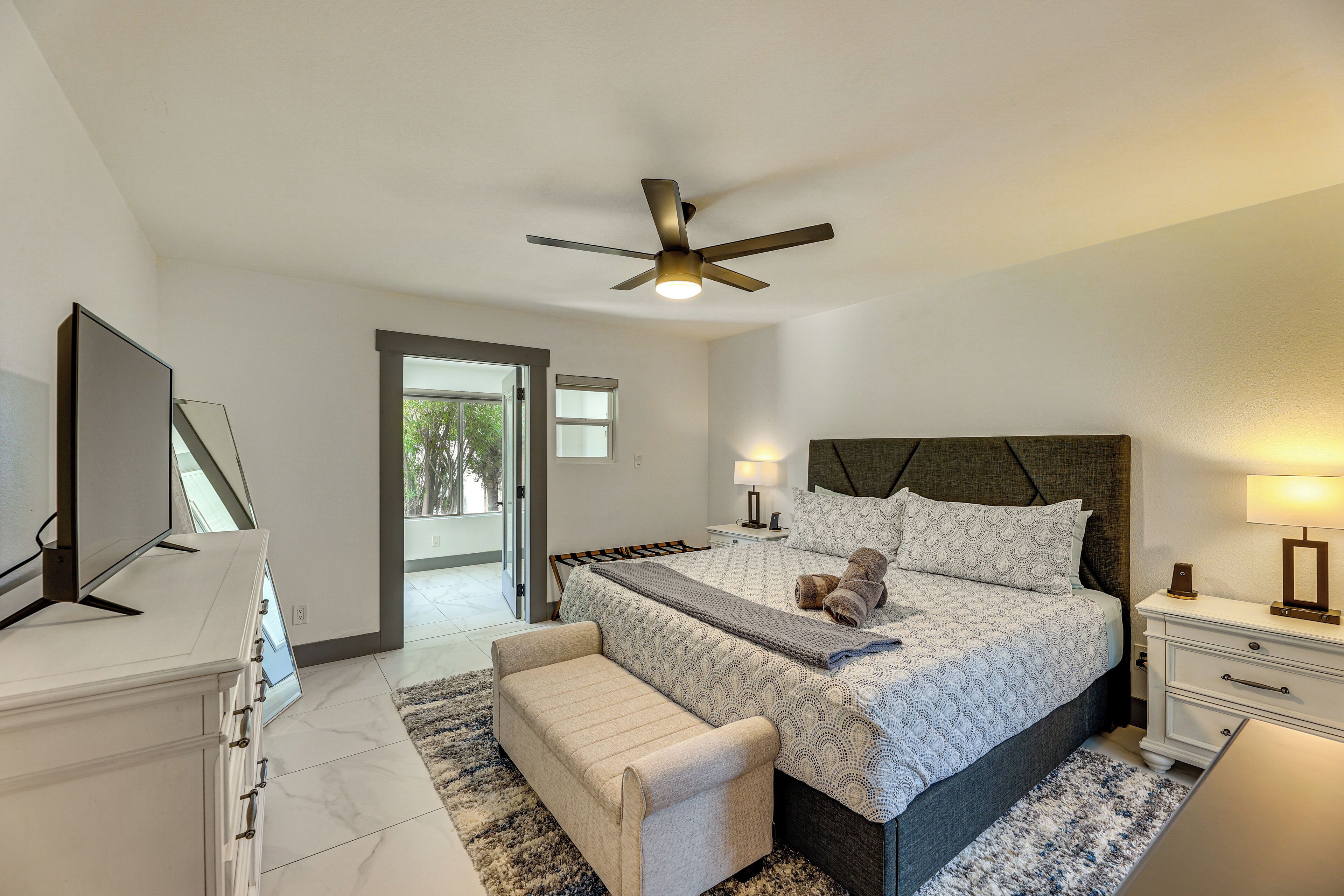 A modern bedroom with a bed, bedside tables, a TV, and a ceiling fan.