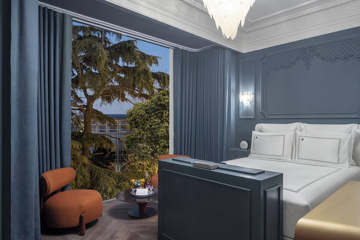 Une chambre d’hôtel avec un lit, un bureau, une chaise et une vue sur des arbres et un pont.