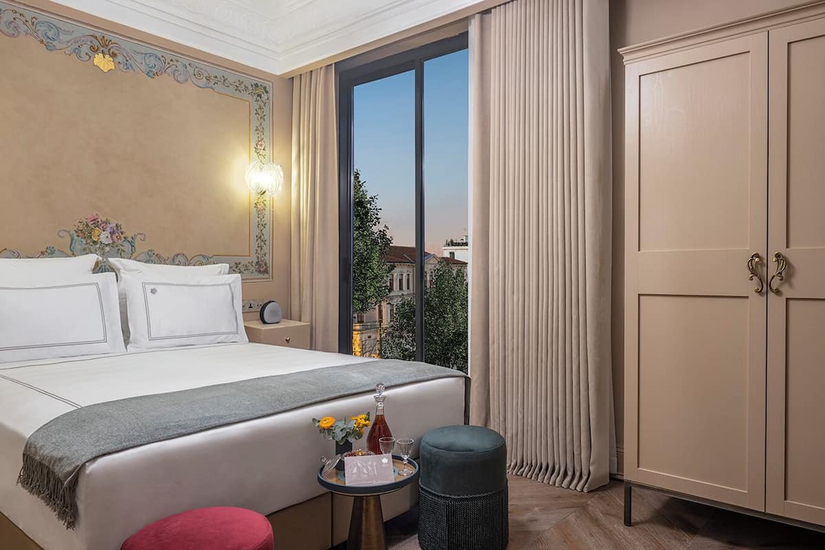 Une chambre d’hôtel avec un grand lit, une petite table sur laquelle est posé un vase de fleurs, une table de chevet et une armoire.