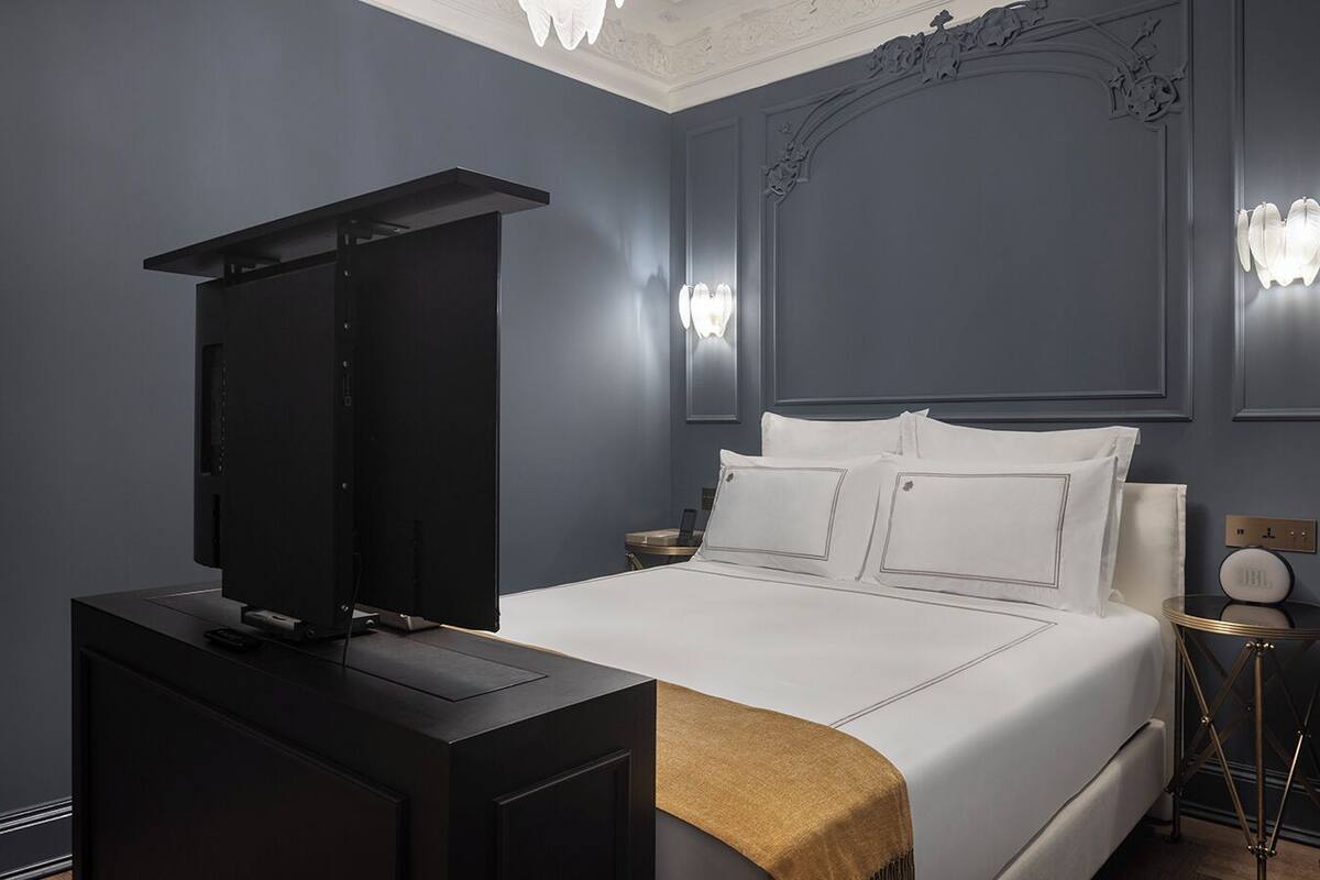 Une chambre d’hôtel moderne dotée d’un grand lit, d’un téléviseur à écran plat, d’une table de chevet et d’un luminaire fixé au mur.