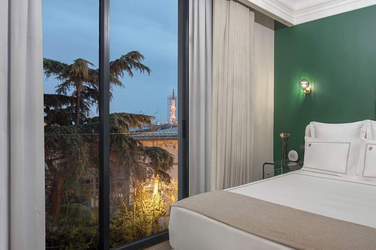 Une chambre d’hôtel avec un grand lit, une vue sur le paysage urbain et un mur d’accent vert.