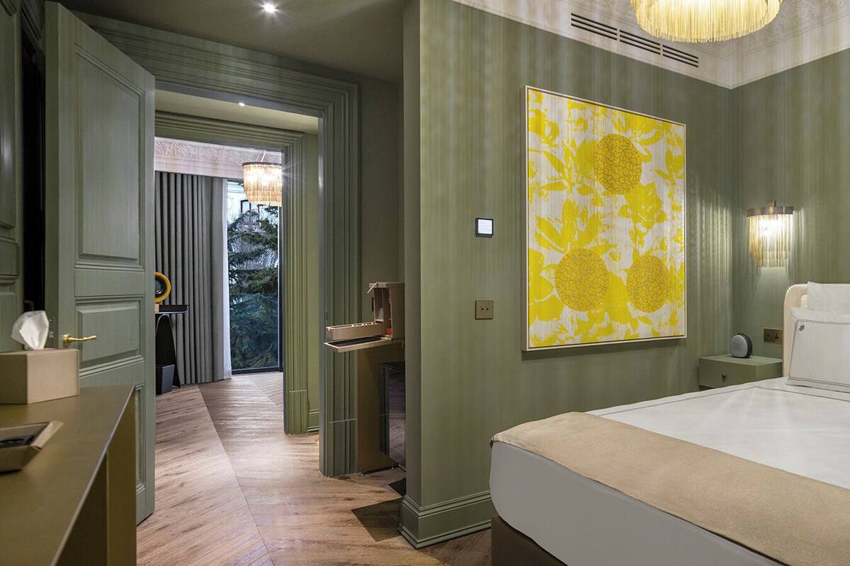 Une chambre d’hôtel avec un grand lit, une table de chevet, une commode, une lampe fixée au mur et un grand tableau abstrait.