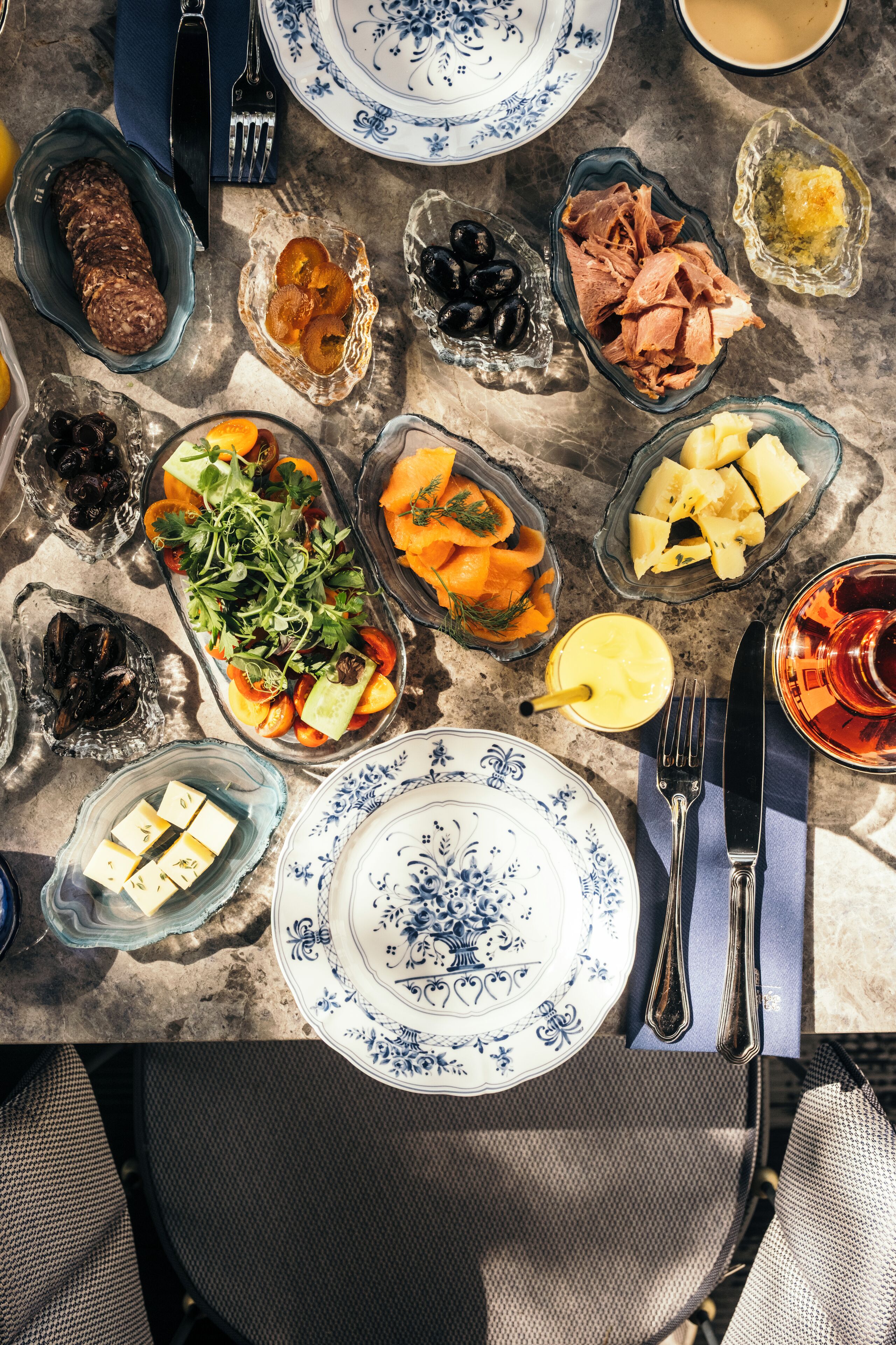 A table set with various dishes, including a salad, cheese, and meats, on a marble table.