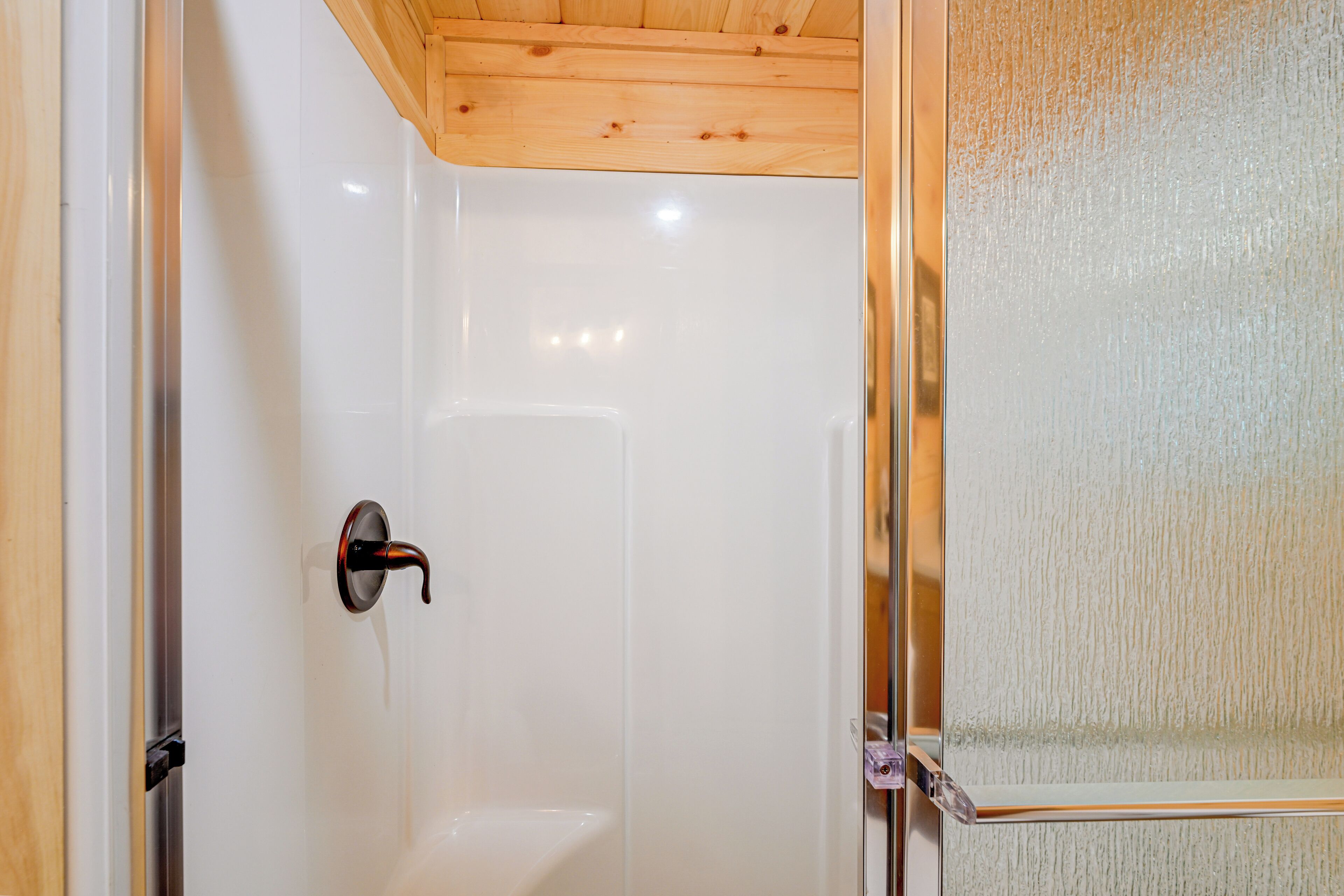A shower with a wooden ceiling and a glass door.