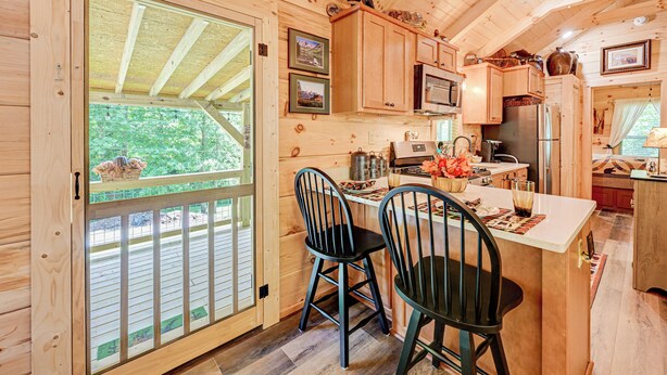 A wooden cabin kitchen with a dining area, wooden cabinets, and a large window overlooking a deck.