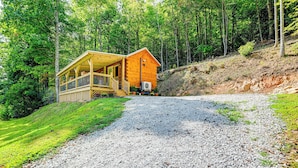 A wooden cabin with a porch, surrounded by a forest.