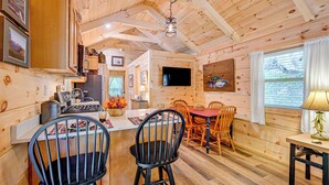 A wooden cabin interior with a kitchen, dining area, and a TV mounted on the wall.