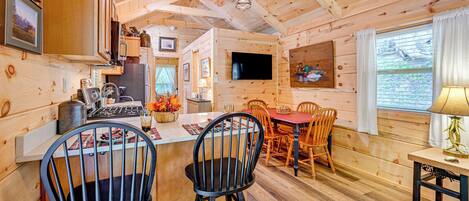 A wooden cabin interior with a kitchen, dining area, and a TV mounted on the wall.