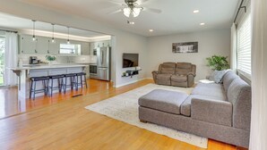 A modern living room with a grey sofa, a ceiling fan, and a kitchen area with a bar stool. - Wooster Family Home w/ Yard & Fire Pit! (Wooster)