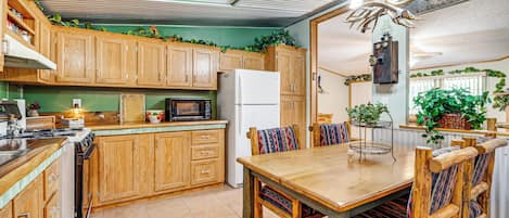 A kitchen with wooden cabinets, a dining table with chairs, a refrigerator, and various plants.
