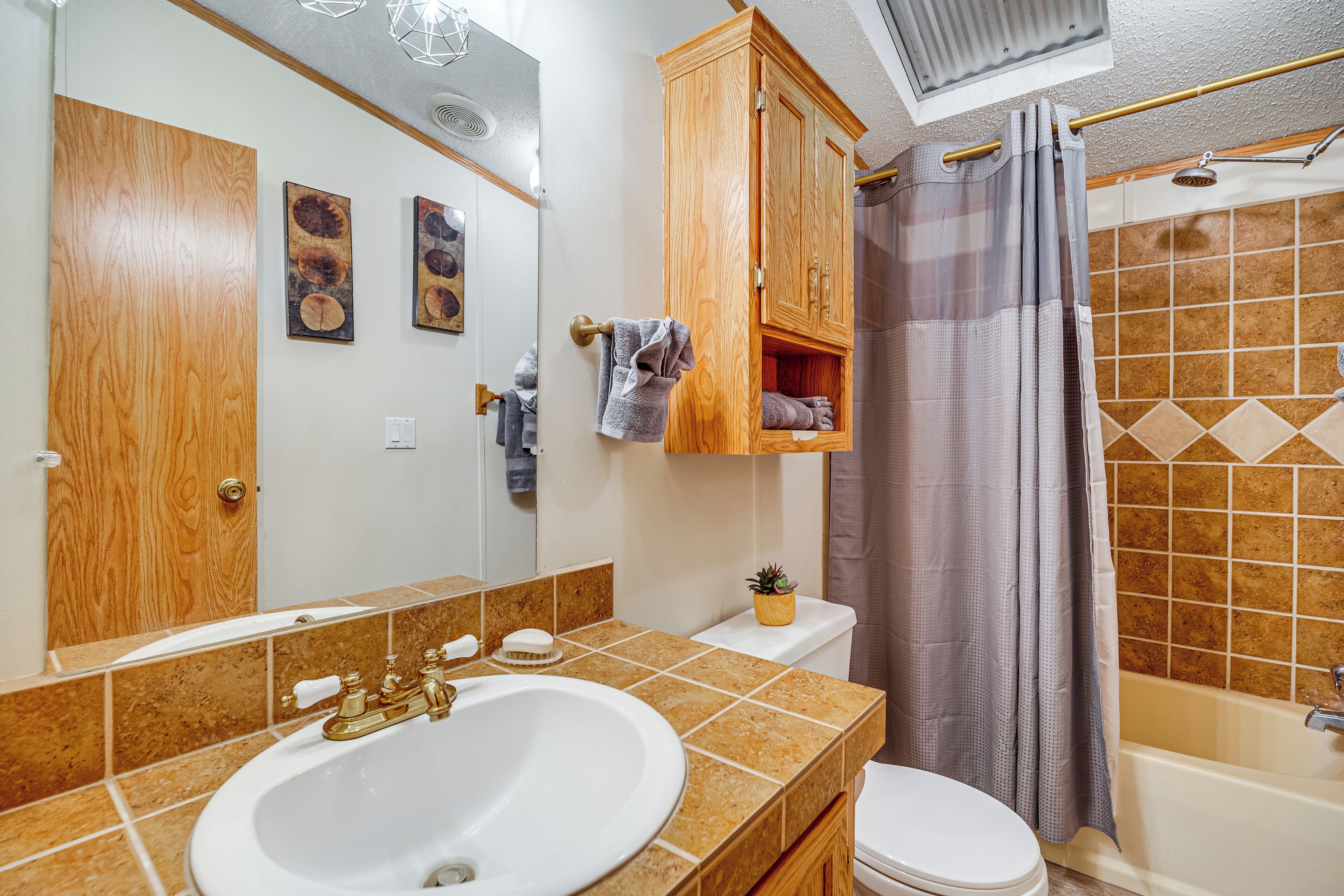 A bathroom with a wooden cabinet, a sink, a toilet, and a shower area.