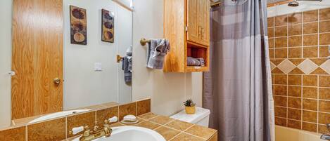 A bathroom with a wooden cabinet, a sink, a toilet, and a shower area.
