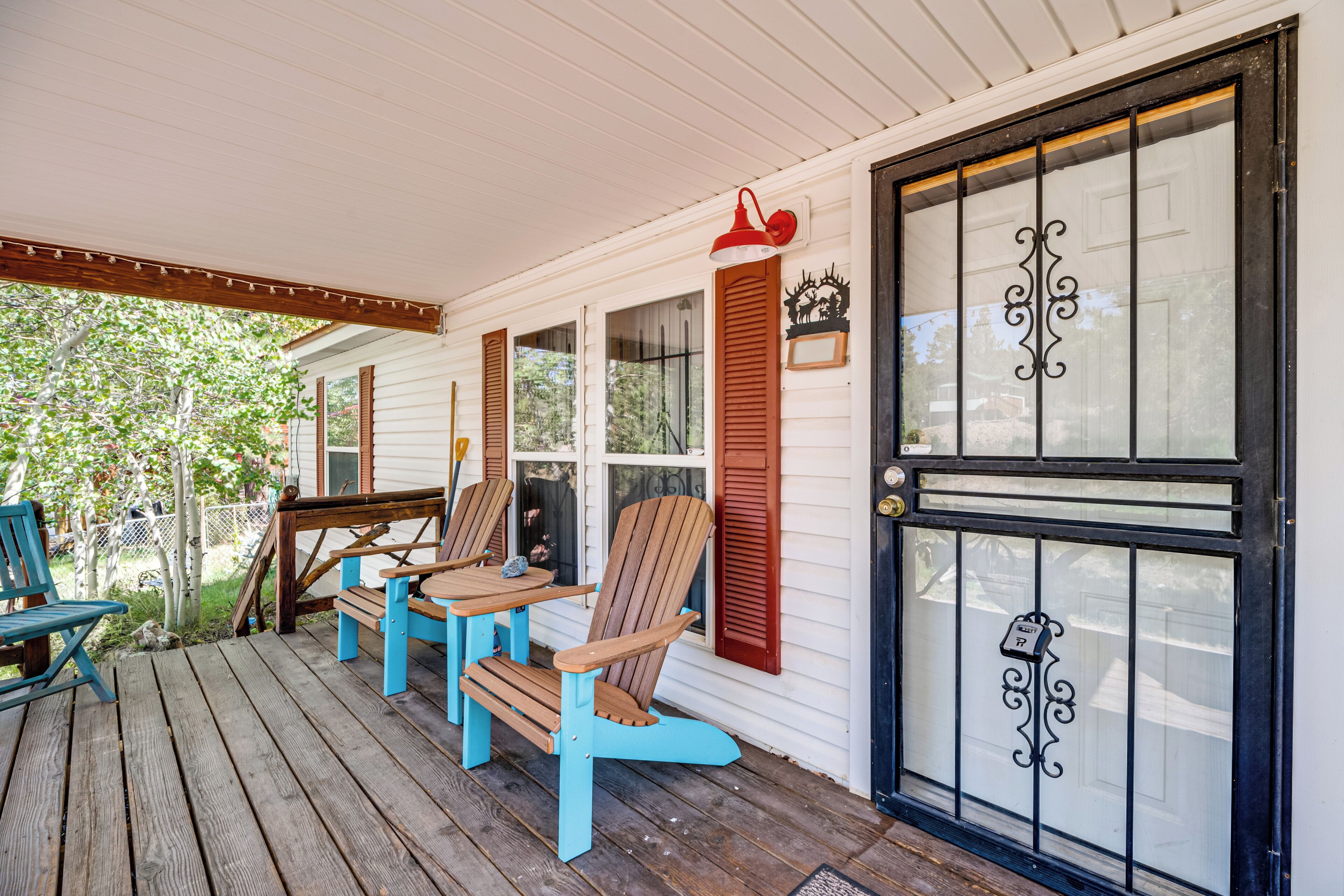 A wooden porch with three Adirondack chairs and a table, a black door with a decorative glass panel, and a small sign on the door.