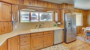 A kitchen with wooden cabinets, a stainless steel refrigerator, a sink, and a window overlooking a residential area. - Walk to Downtown: Brigham City Family Home (Brigham City)