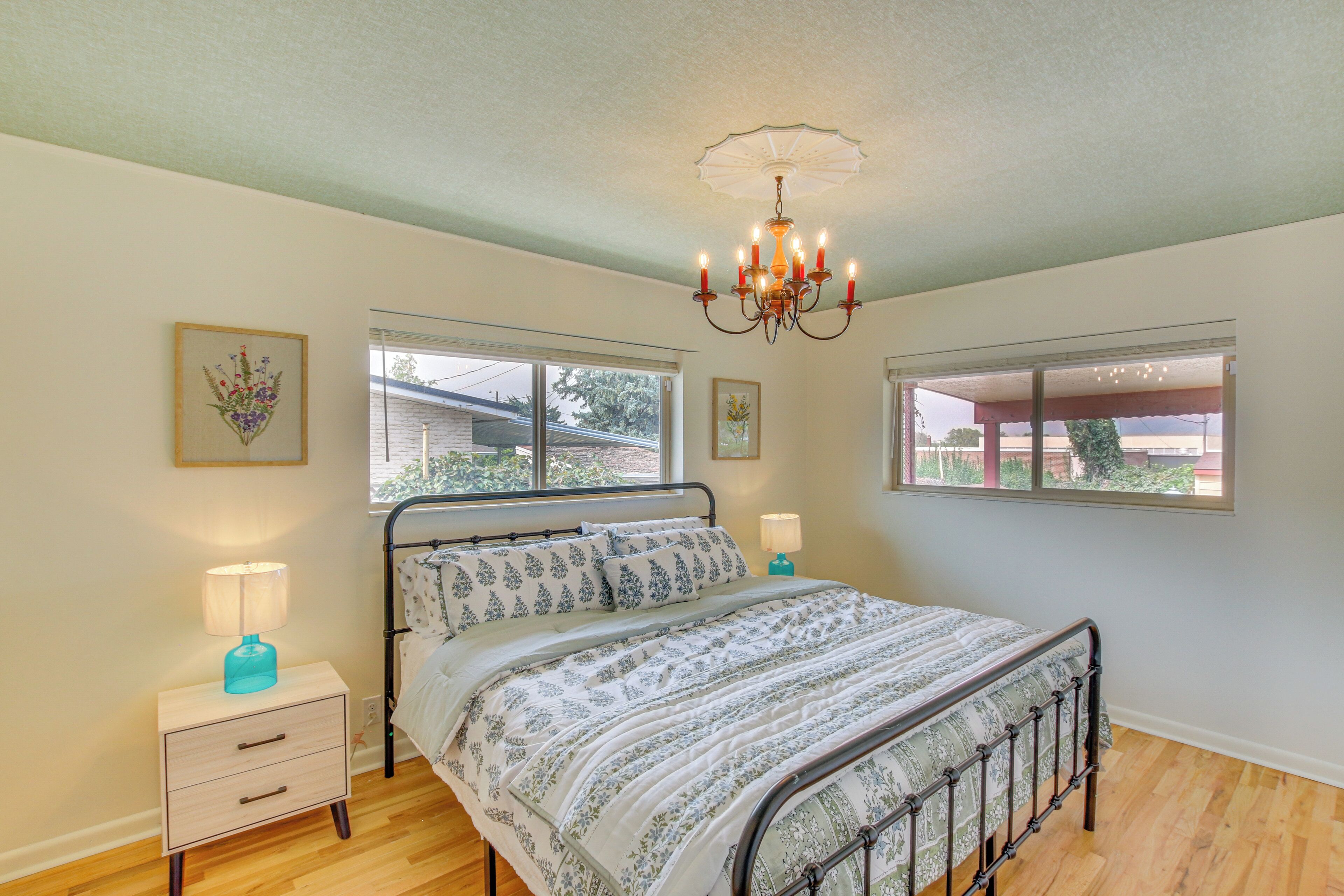 A bedroom with a metal bed frame, a bedside table with a lamp, and a chandelier.