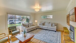 A spacious living room with a large window, a chandelier, a fireplace, and a cozy seating area. - Walk to Downtown: Brigham City Family Home (Brigham City)