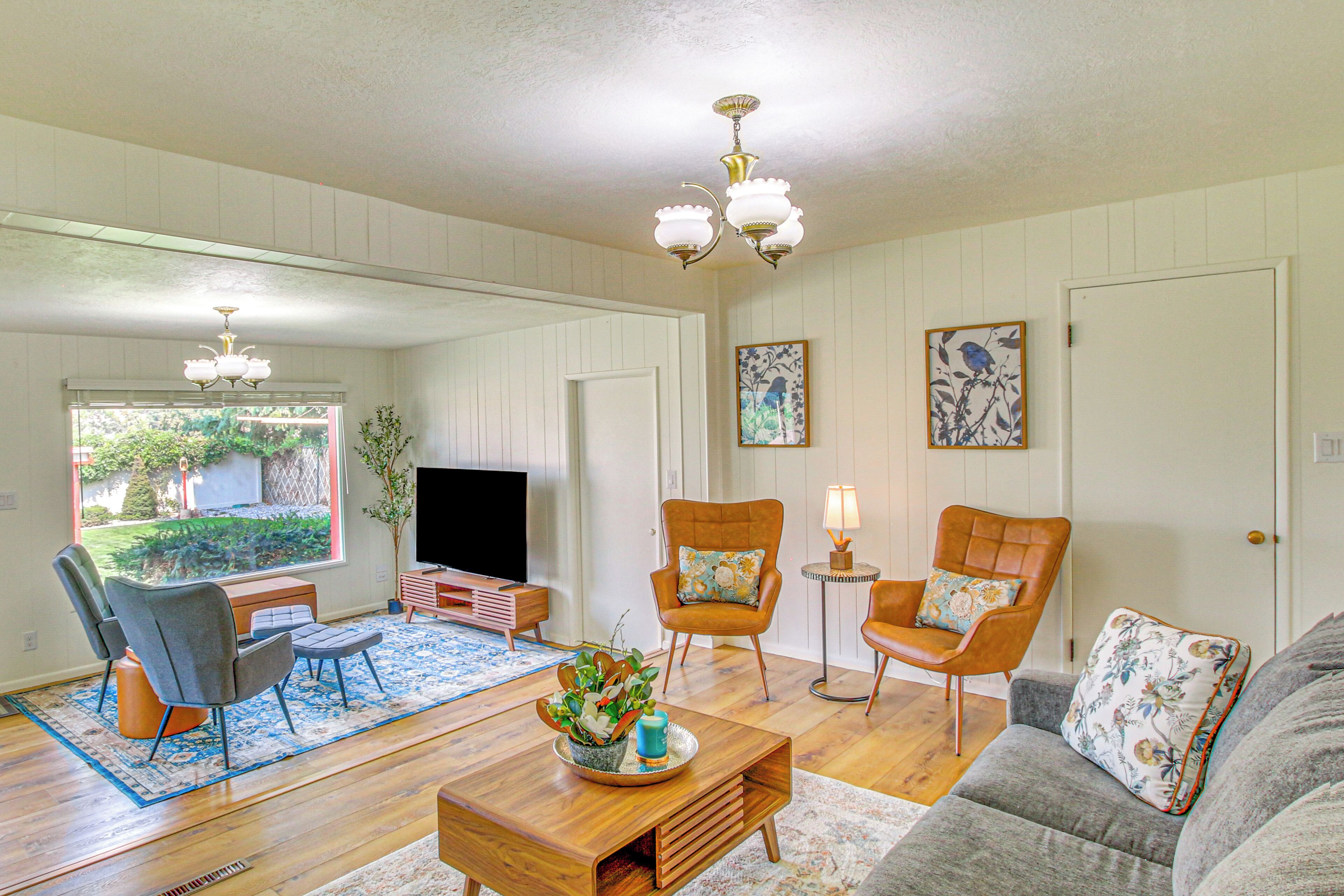 A living room with a wooden coffee table, two armchairs, a sofa, a TV, and a chandelier.