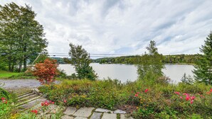 A lakeside view with a stone pathway leading to a wooden deck, surrounded by lush greenery and flowers. - Home w/ Private Dock Near Colgate University (Hamilton)