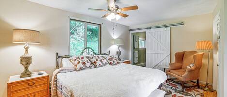 A bedroom with a bed, nightstand, chair, and ceiling fan.