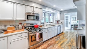 A modern kitchen with white cabinets, a stainless steel stove, and a large window. - Home w/ Private Dock Near Colgate University (Hamilton)