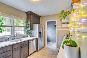 A modern kitchen with a stainless steel refrigerator, a dishwasher, and a sink. There are potted plants on the counter and a window with blinds. - 1 Mi to Valley Junction: Pet-friendly Iowa Home (West Des Moines)
