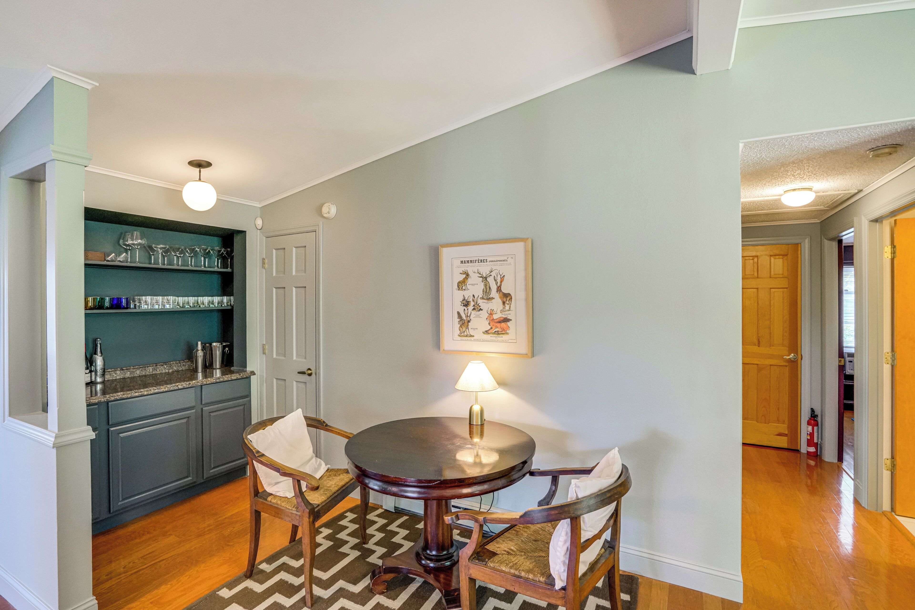 A dining area with a round table, chairs, a lamp, and a wall-mounted picture.